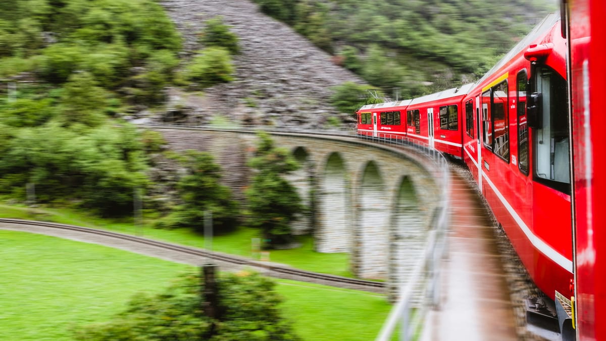 A red Rhaetian Railway train curves onto the stone arches of the Brusio spiral viaduct, seen from the train window.