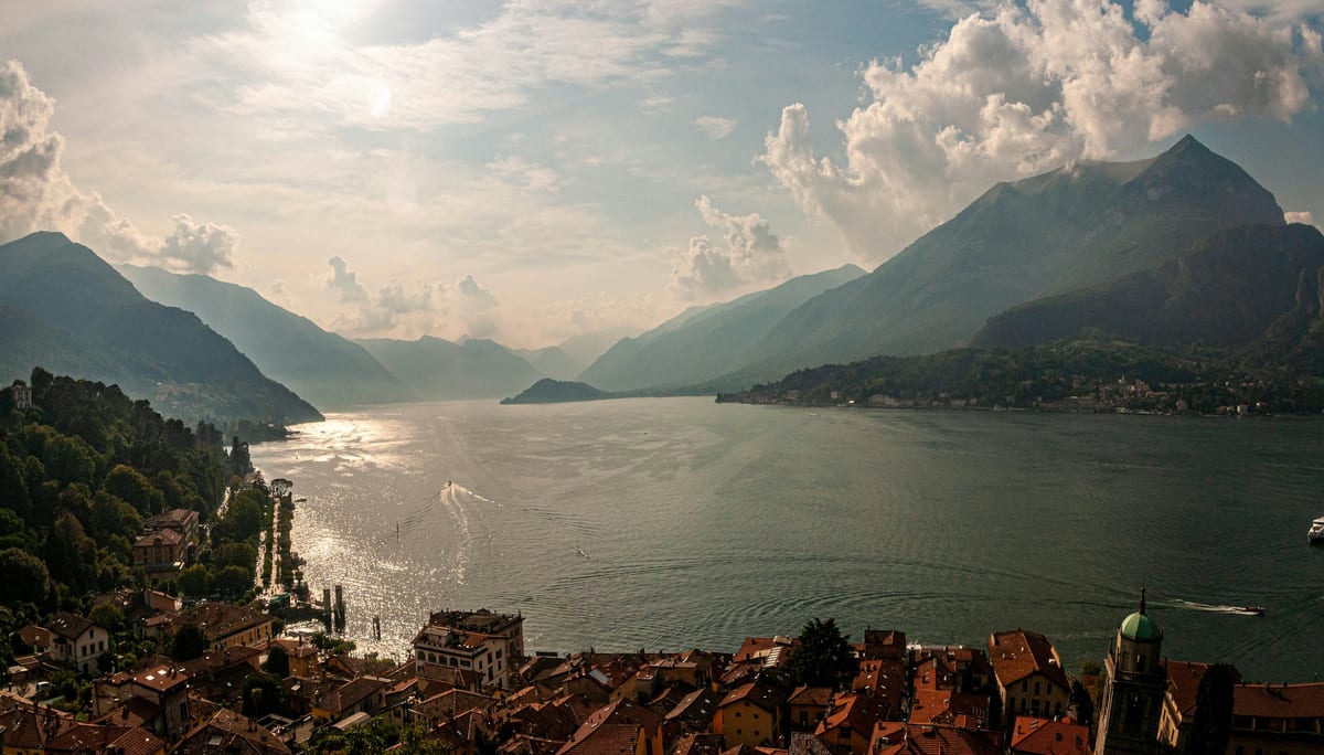 Lake Como seen from above the rooftops of Bellagio, with boats on the water and mountains fading into the haze.