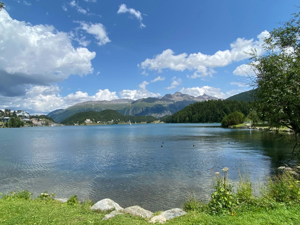 Lake St. Moritz on a sunny summer day, with small sailing boats, forested shores and mountains under scattered cloud.