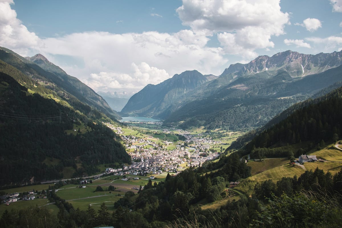 The Poschiavo valley from above: the town of Poschiavo spreads across green meadows, with Lake Poschiavo and mountains beyond.